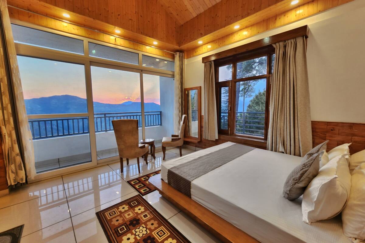 Un dormitorio amplio con una cama grande, techo de madera y un balcón con vistas panorámicas a la montaña.