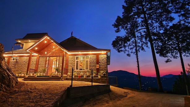 Un edificio de piedra con un porche de madera y vistas a la montaña al atardecer.