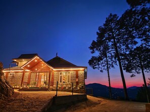 A stone building with a wooden porch and a view of the mountains at dusk. - The Morel House (Kumharsain)