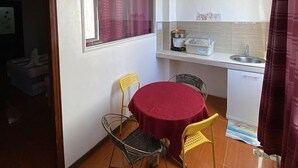 Eine kompakte Küche mit Essbereich, inklusive eines runden Tisches mit zwei Stühlen, einem Fenster mit Vorhängen und einer Küchenzeile mit Spüle und Herd.