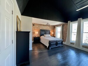 Een slaapkamer met een bakstenen muur, een bed, een nachtkastje en een dressoir.