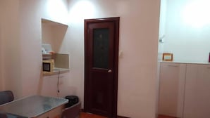 A small, compact room with a dining table and chairs, a microwave, a cabinet, and a door with a frosted glass panel.