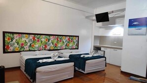 A hotel room with two beds, a large floral artwork on the wall, a flat-screen TV, and a kitchenette.