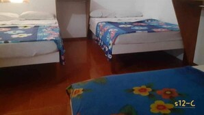Une chambre avec deux lits simples, chacun agrémenté d’une couvre-lit à motifs floraux, d’une petite table de chevet et d’un miroir fixé au mur.