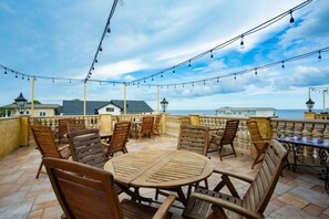 A terrace with wooden furniture and string lights, overlooking a coastal area with buildings and a view of the sea. - A Romantic Haven by the Shore (St Simons Island)