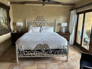 A large bed with ornate metal headboard and footboard, two bedside lamps, and a view of outdoor furniture through a large window. - A Romantic Haven by the Shore (St Simons Island)