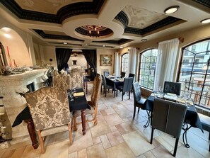A dining area with patterned chairs, a fireplace, and a view through large windows. - A Romantic Haven by the Shore (St Simons Island)