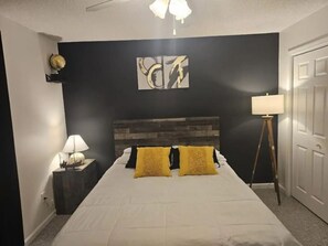 Un dormitorio con cama, mesita de noche, lámpara y puerta.
