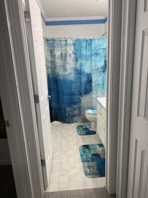 Un baño con cortina de ducha, inodoro y dos alfombras azules en el suelo.