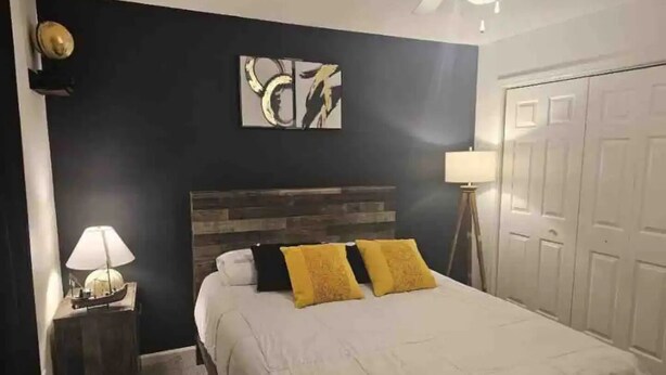 A bedroom with a bed, a nightstand, a lamp, and a door.