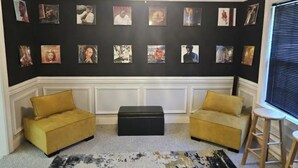 A room with a black wall adorned with framed pictures, two yellow sofas, a black ottoman, a black and white rug, and a ceiling fan.