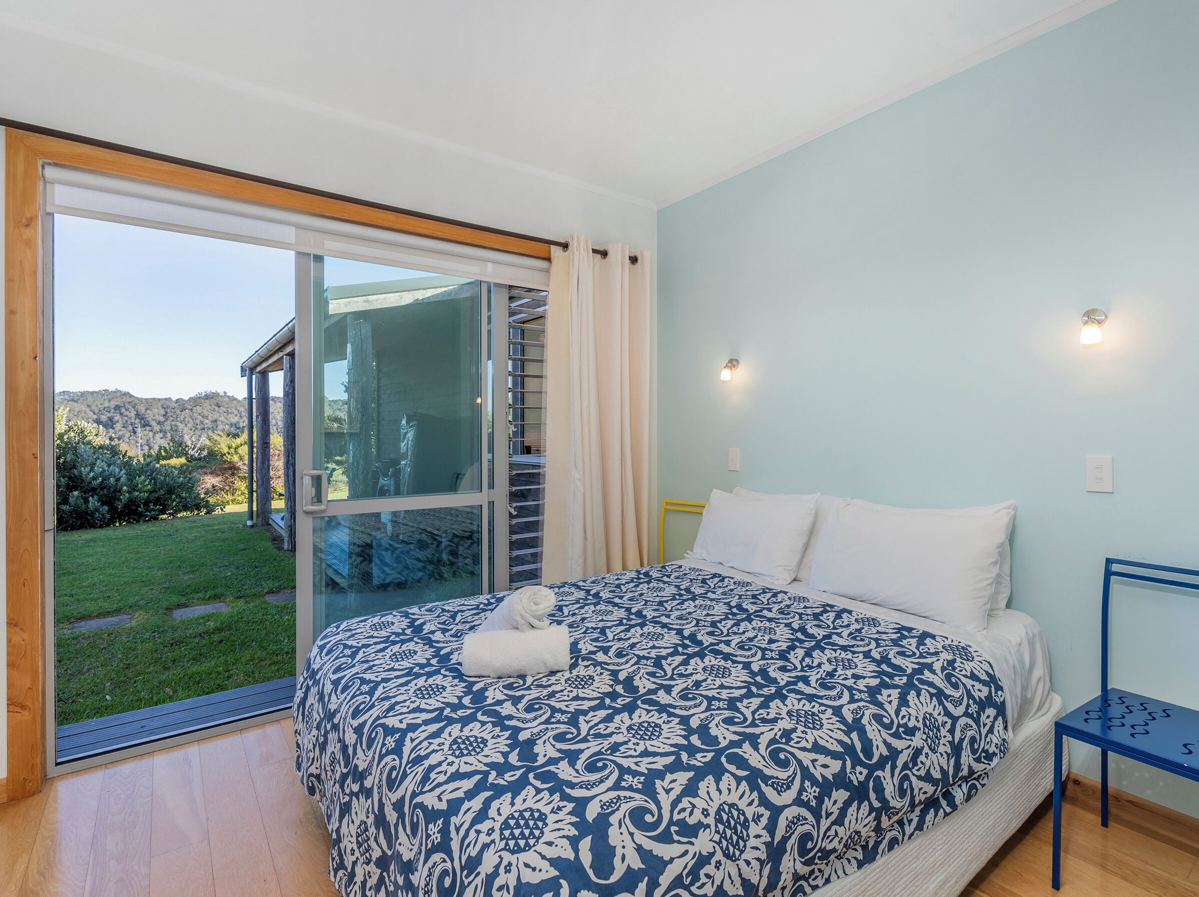 A bedroom with a large bed, a view of the outdoors through a sliding glass door, and a small table by the bed.