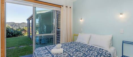 A bedroom with a large bed, a view of the outdoors through a sliding glass door, and a small table by the bed.