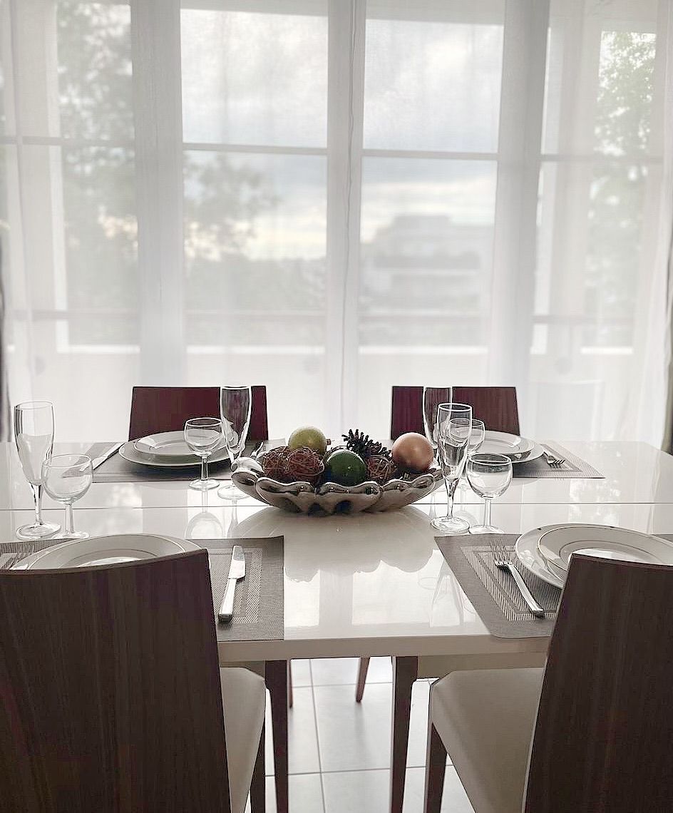 A dining table set for four with chairs, a bowl of fruit, and wine glasses.