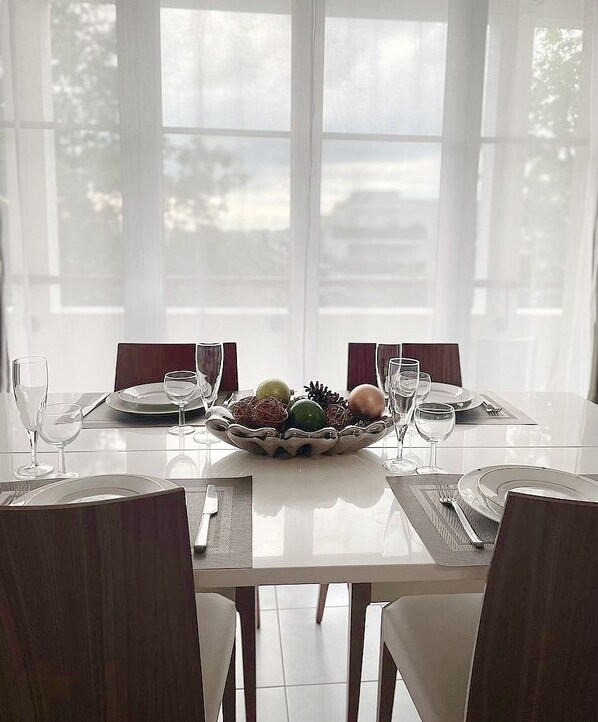 Mesa de comedor preparada para cuatro personas, con sillas, un cuenco de fruta y copas de vino.