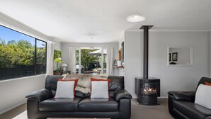 Un salon moderne avec un canapé en cuir noir, une cheminée et une grande fenêtre donnant sur l’extérieur.