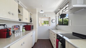 Une cuisine de taille réduite, avec des meubles blancs, un grille-pain rouge et une fenêtre donnant sur un paysage verdoyant.