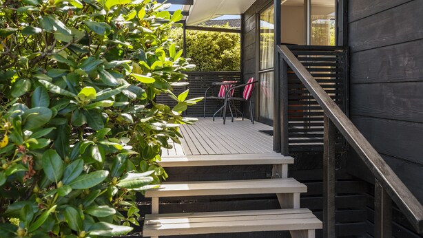 Une terrasse en bois avec un escalier menant à un espace abrité comprenant une table et des chaises.