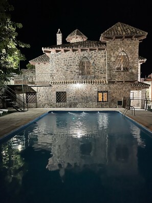 Un bâtiment en pierre avec une piscine, de nuit.