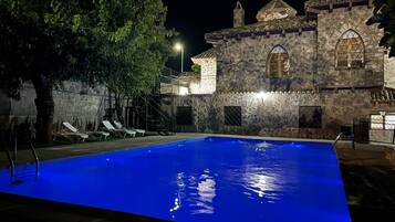 Un edificio de piedra con piscina y sillas de descanso.