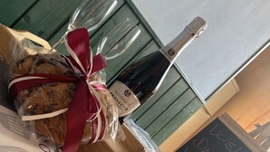Una mesa con una botella de vino, una copa y una galleta envuelta en una cinta roja. Un letrero de pizarra dice “¡Bienvenida, cariño, feliz día!”