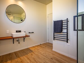 Een badkamer met een houten vloer, een wit wastafelmeubel met spiegel erboven en een handdoekhouder met handdoek.
