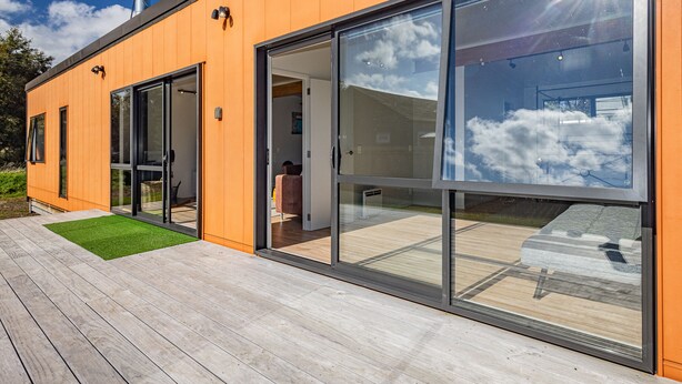 Une maison moderne dotée de grandes portes vitrées, d’une terrasse en bois et d’une cheminée.