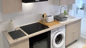 A modern kitchen with a built-in oven, a washing machine, a black range hood, and wooden cabinets. - « Modern Cosy » Hyper Centre Bernay (Bernay)
