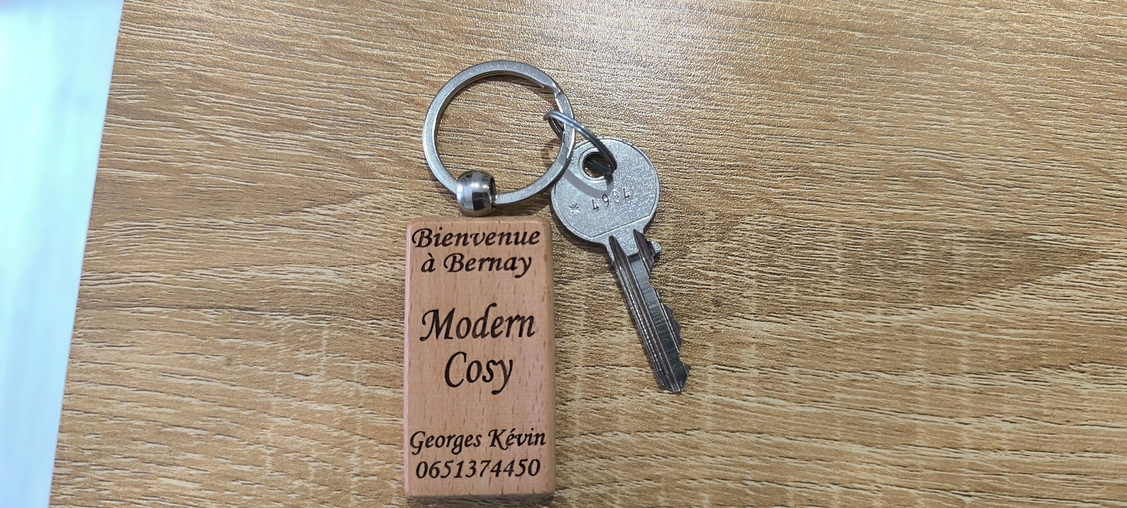 A keychain with a wooden tag that reads "Bienvenue à Bernay Modern Cosy Georges Kevin 0651374450."