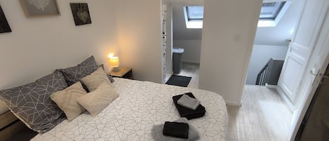 Een slaapkamer met een bedovertrek met een geometrisch patroon, een bedlamp en uitzicht op een trap die naar een verdieping leidt.
