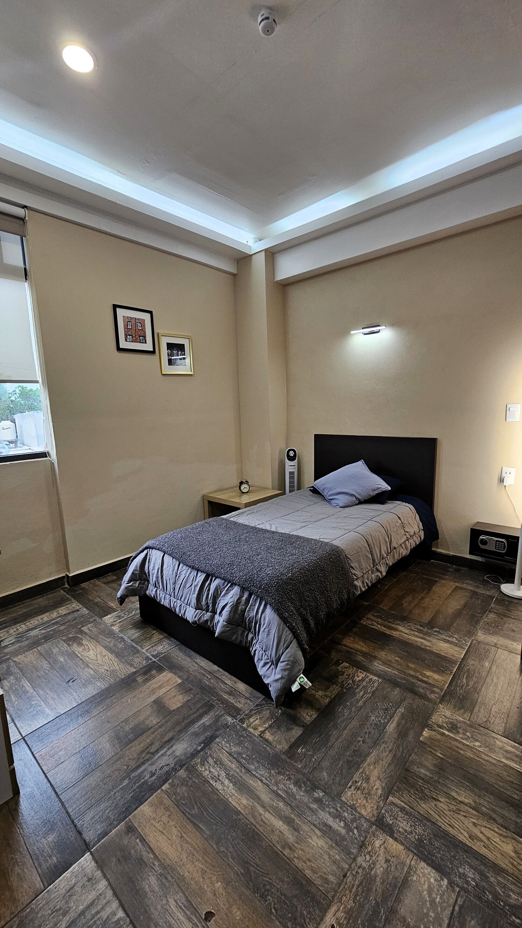 Un dormitorio con cama, mesitas de noche, un calentador y una ventana.