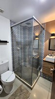 A bathroom with a glass-enclosed shower, a toilet, a sink, and a mirror.