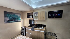A compact kitchen with a built-in microwave, a coffee maker, and a sink. A flat-screen TV is mounted on the wall, displaying a menu interface. - A07 SUPER CITY SUITES AT PLAZA ACEQUIA (Cuautitlan Izcalli)