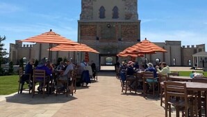 An outdoor dining area with tables and chairs under orange umbrellas, in front of a historic building with a tower. - Middle Bass Island retreat,10-min ferry ride to Put-in-Bay, Pet friendly! (Middle Bass)