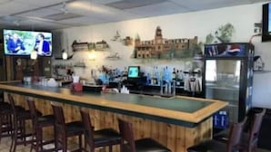 A bar area with a long counter, multiple bar stools, a television screen, and a wall mural depicting a building. - Middle Bass Island retreat,10-min ferry ride to Put-in-Bay, Pet friendly! (Middle Bass)