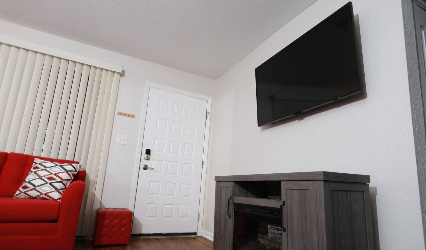 Ein Zimmer mit einer weißen Tür, einem roten Sessel, einem an der Wand befestigten Fernseher und einem kleinen Schrank.