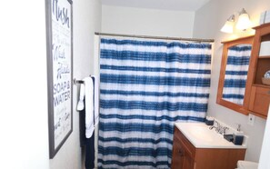 Een badkamer met een gestreept douchegordijn, een wastafel, een spiegel en een handdoek aan de muur.