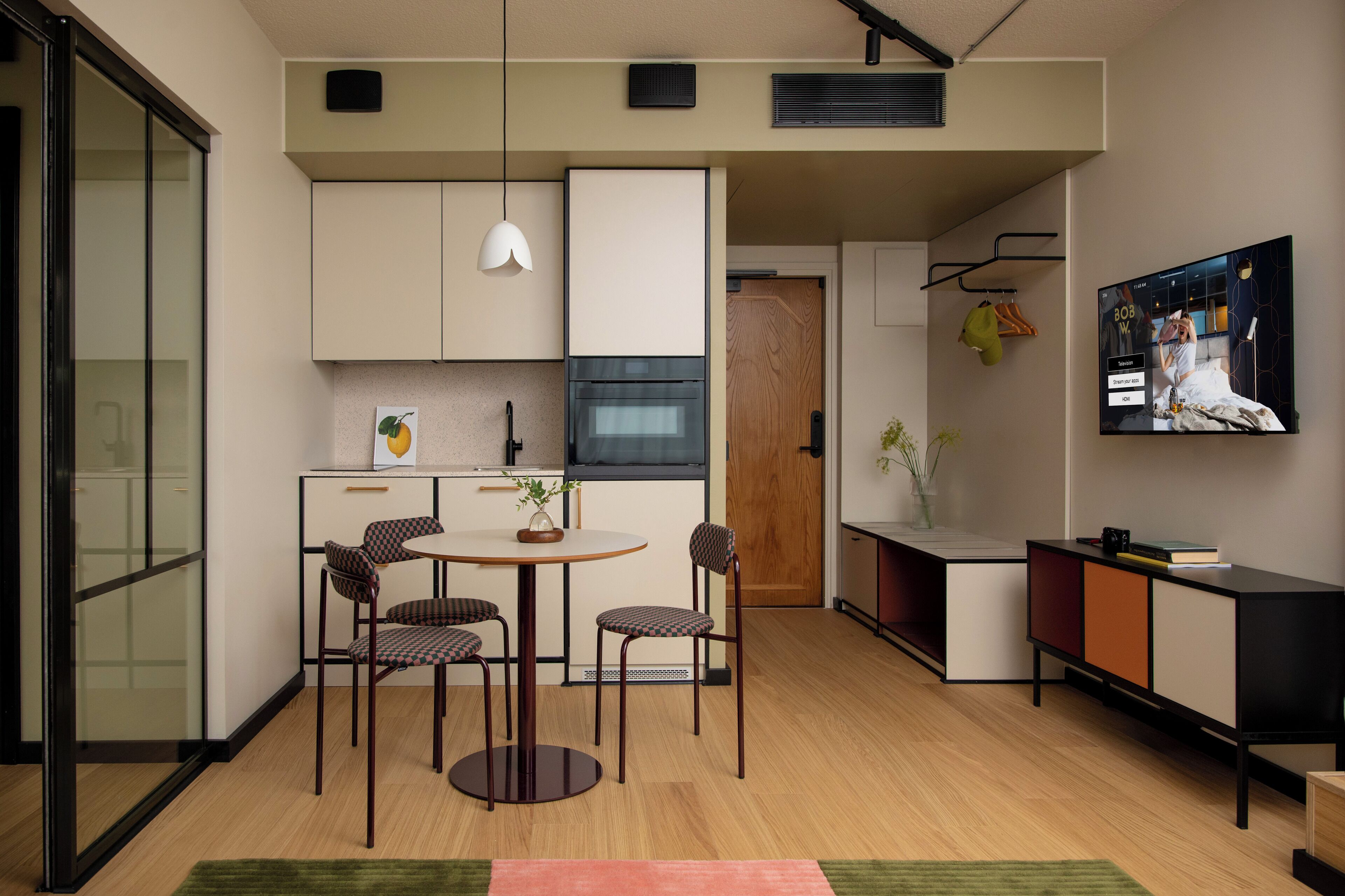 Une cuisine moderne avec un coin repas, un téléviseur fixé au mur et un petit meuble agrémenté d’une plante.