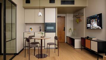 A modern kitchen with a dining area, a TV mounted on the wall, and a small cabinet with a plant.