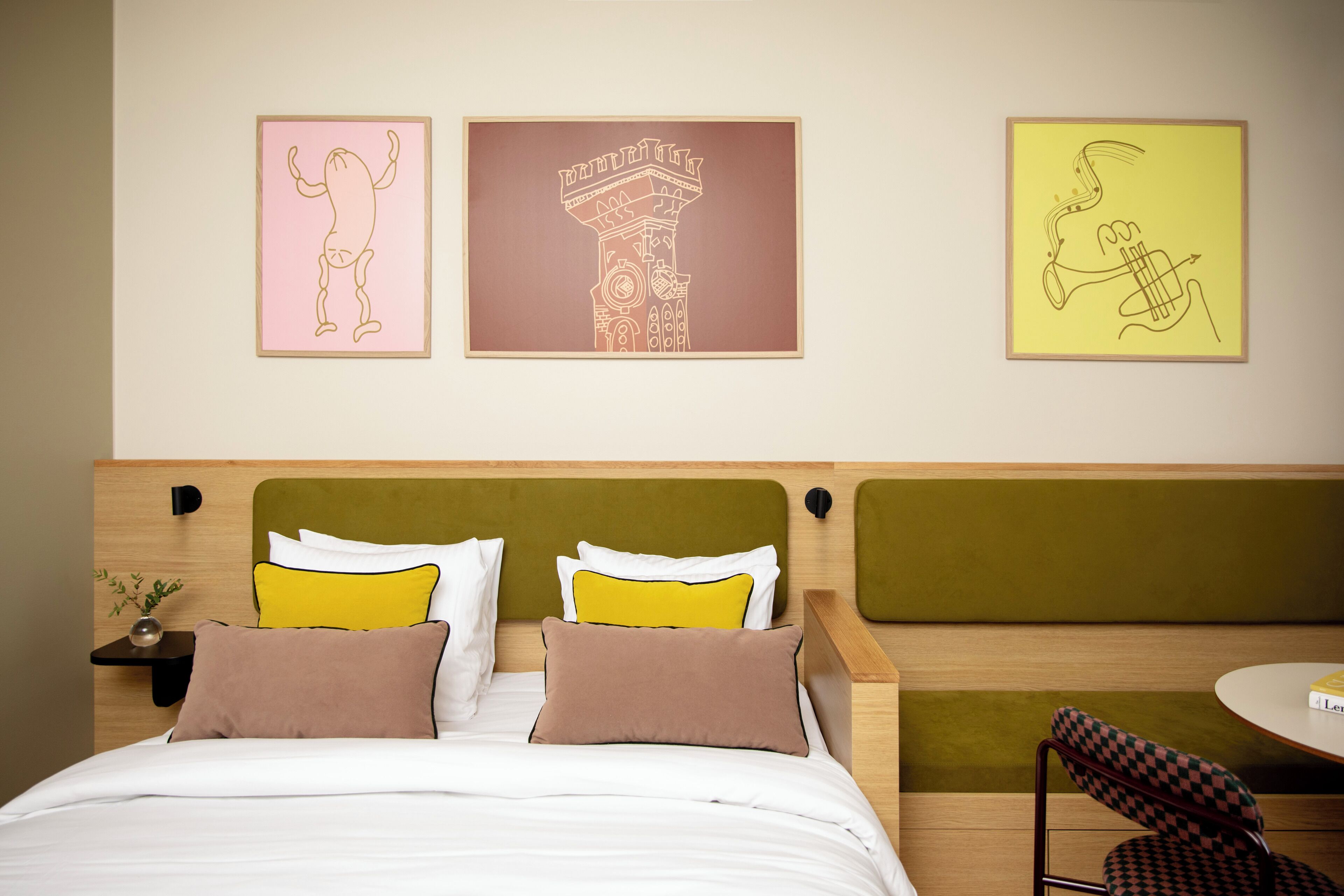 Habitación de hotel con cama, mesita de noche, una silla y tres cuadros en la pared.