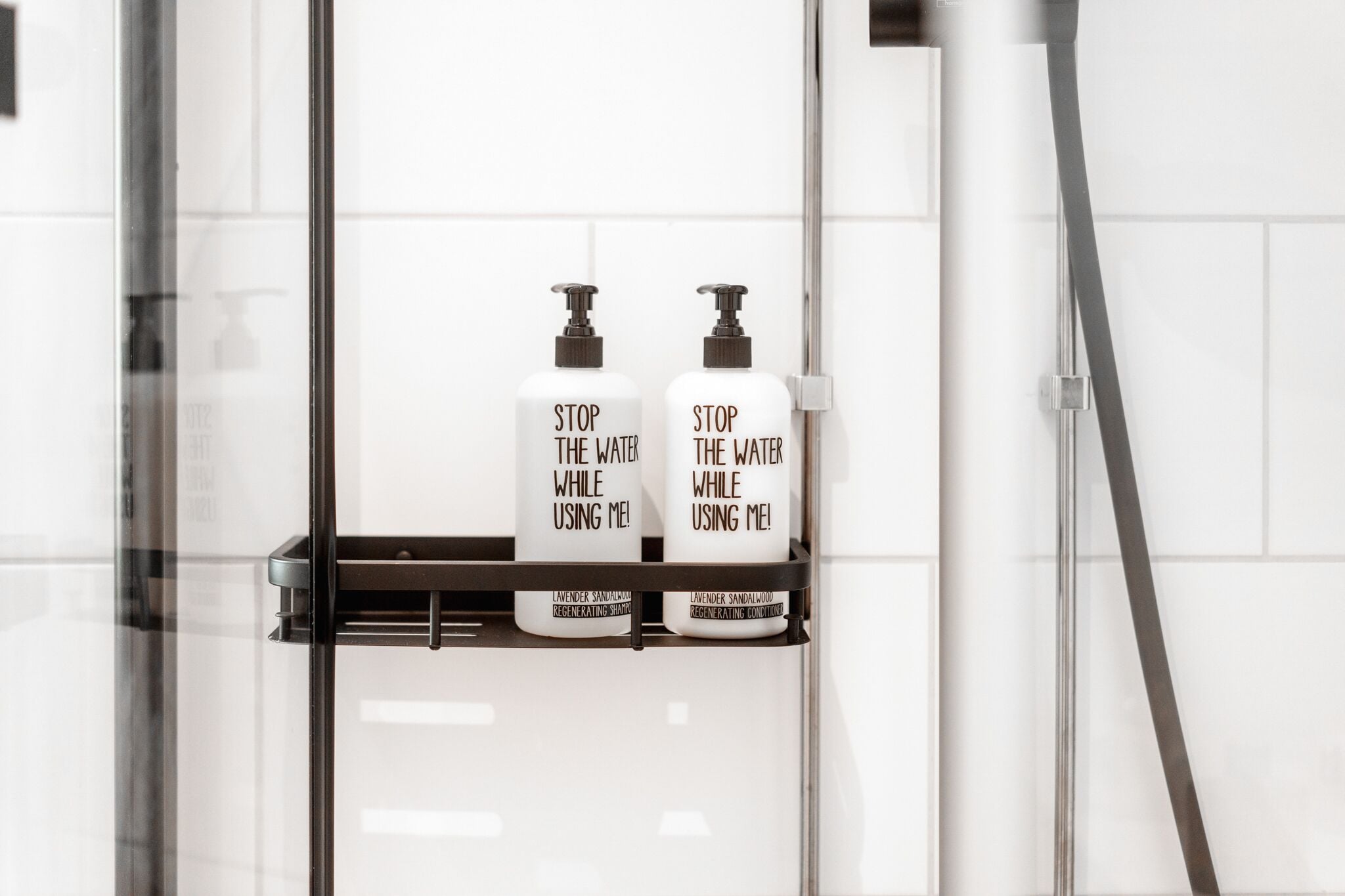 A bathroom with two bottles of 'Stop the Water While Using Me!' shampoo on a shelf.