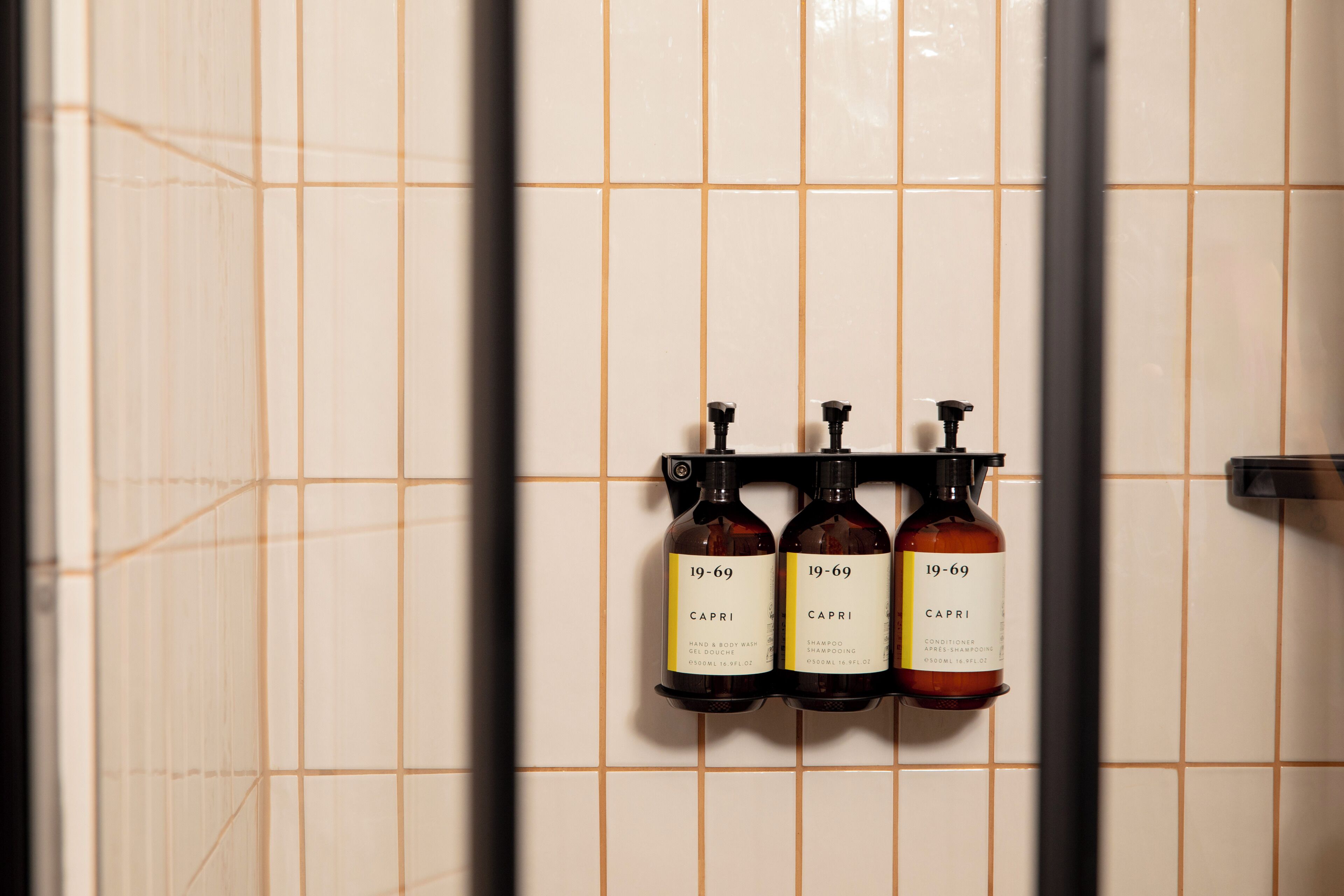 Drei Flaschen Capri Shampoo und Conditioner hängen an einer gefliesten Wand.