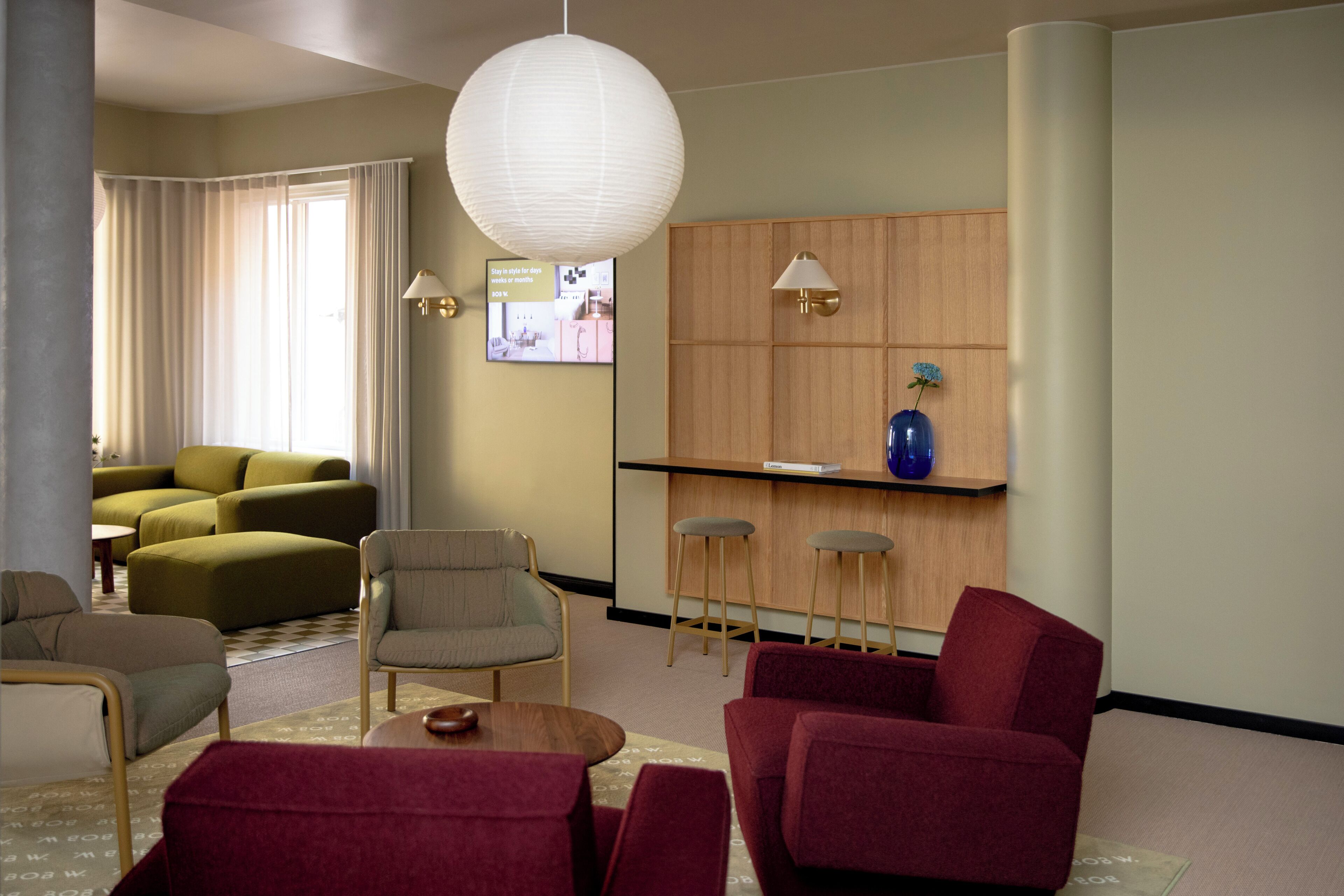 A modern living room with a sofa set, a coffee table, and a red armchair. There is a wooden bar with stools and a blue vase on the wall.