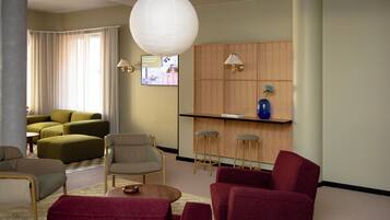 A modern living room with a sofa set, a coffee table, and a red armchair. There is a wooden bar with stools and a blue vase on the wall.