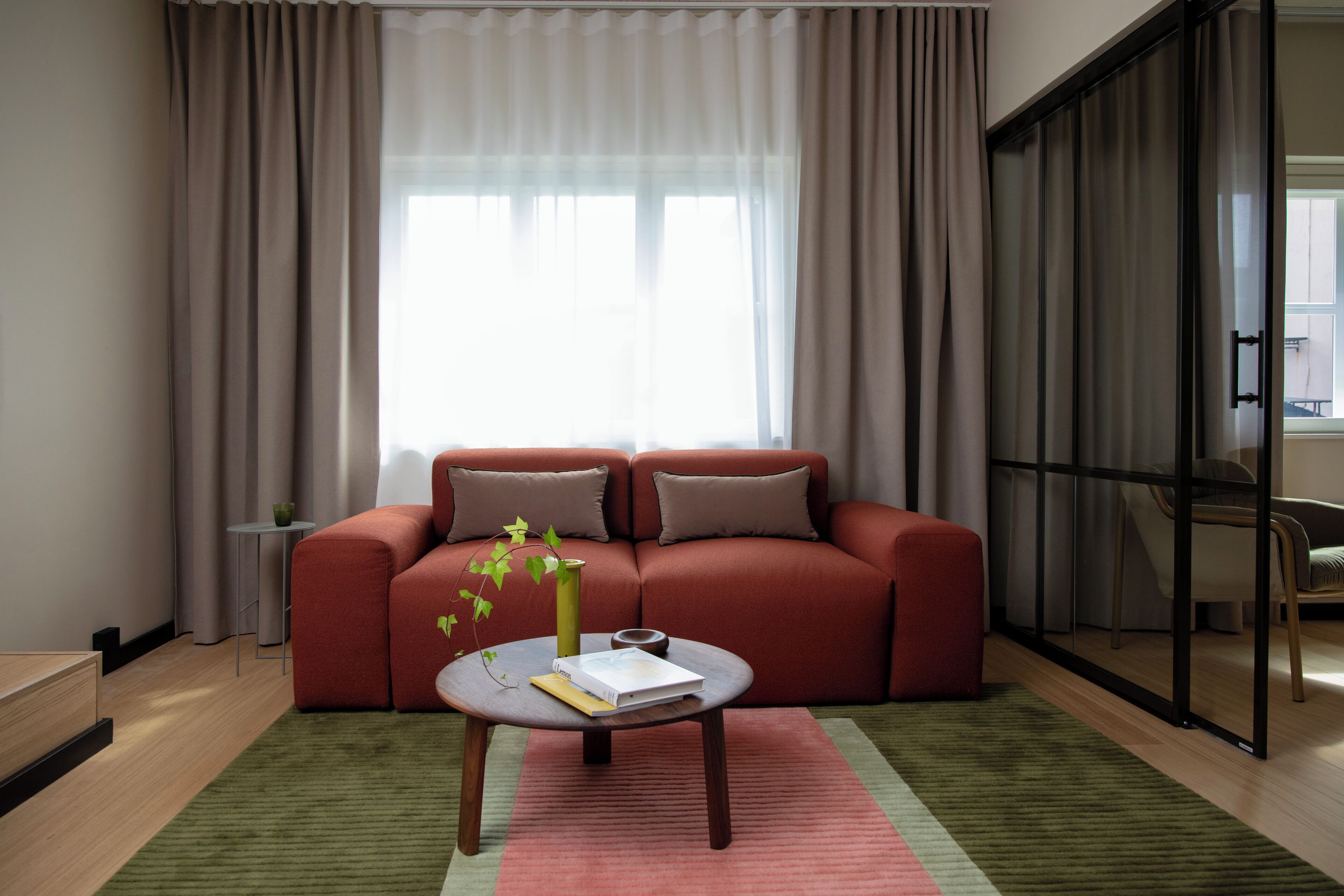 Una sala de estar moderna con un sofá rojo, una mesa de centro redonda con un libro y un florero, y una alfombra verde.