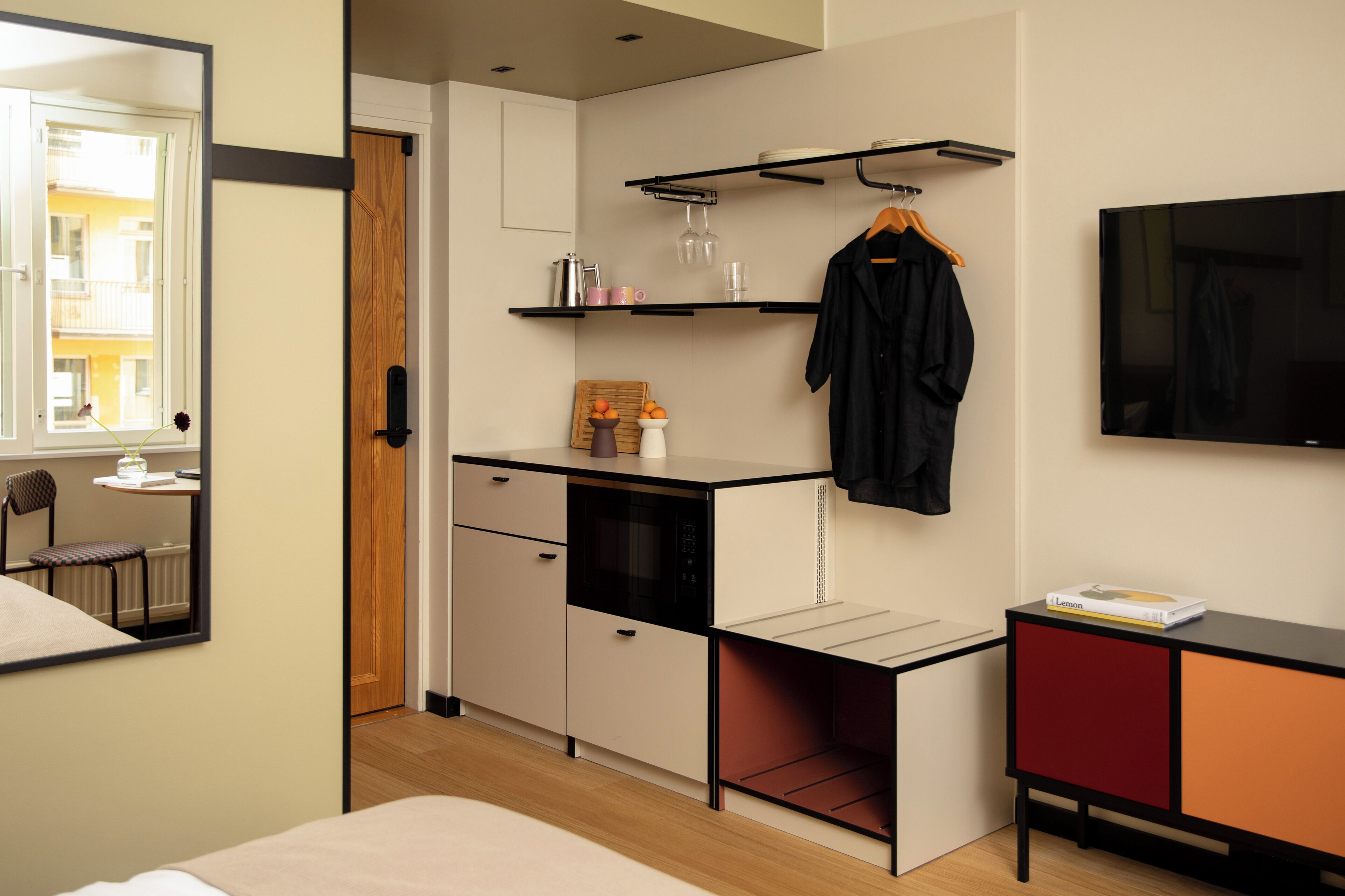 A compact hotel room with a kitchenette, a bed, a TV, and a view of the outside balcony.