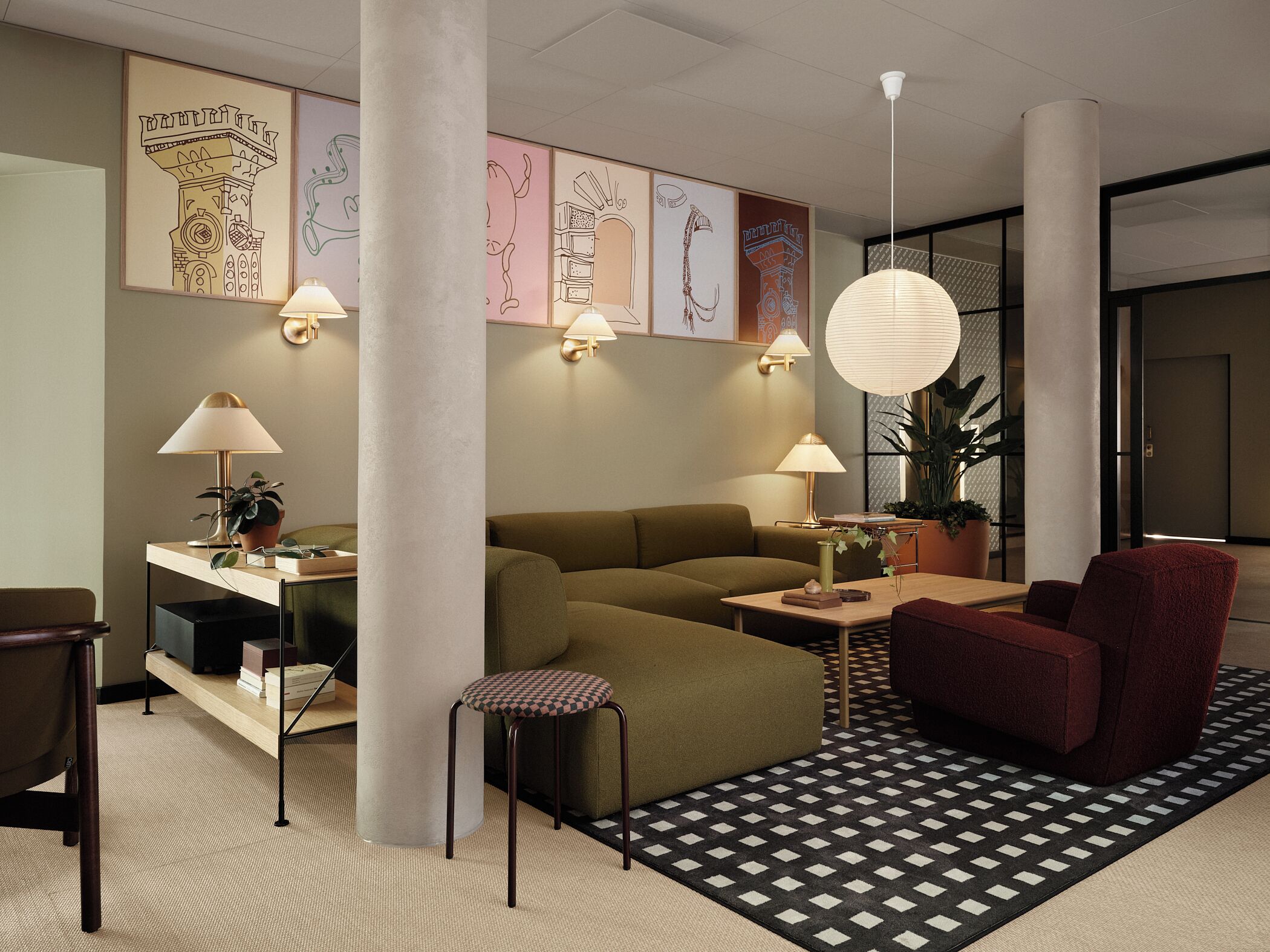 Ein modernes Wohnzimmer mit Sofa, Sessel, Couchtisch und Schreibtisch mit Lampe. An den Wänden befinden sich dekorative Kunstwerke und ein Pendelleuchte.