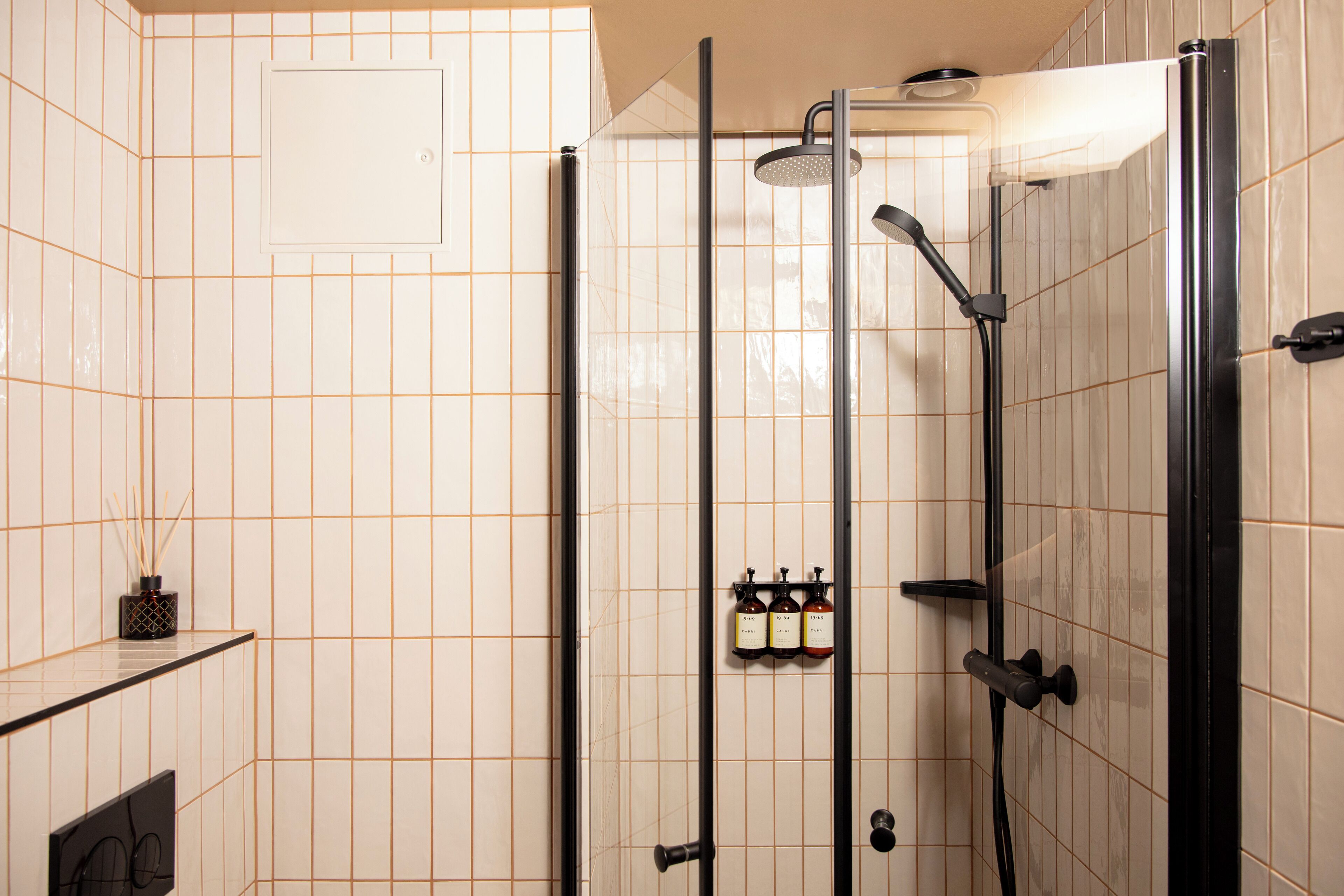A modern bathroom with a walk-in shower, tiled walls, and a shelf with toiletries.