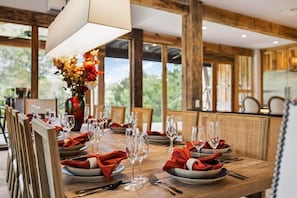 A dining table set for a meal with chairs, a vase of flowers, and a view of the outdoors.
