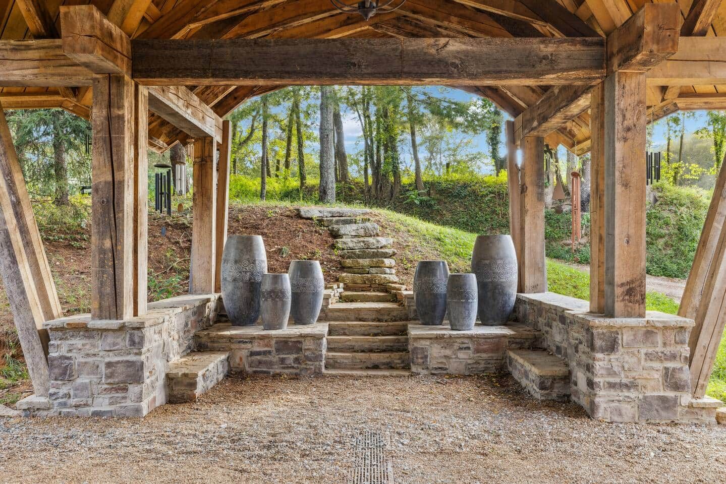 A covered outdoor area with stone steps leading up to a wooden structure, surrounded by trees.
